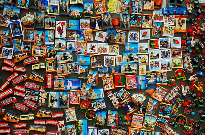 Lots of touristy fridge magnets from various places around the world stuck on a grey background.