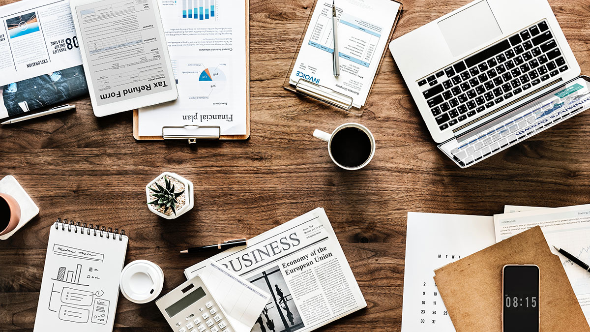 Financial reports, coffee, laptop, and phone on wooden table