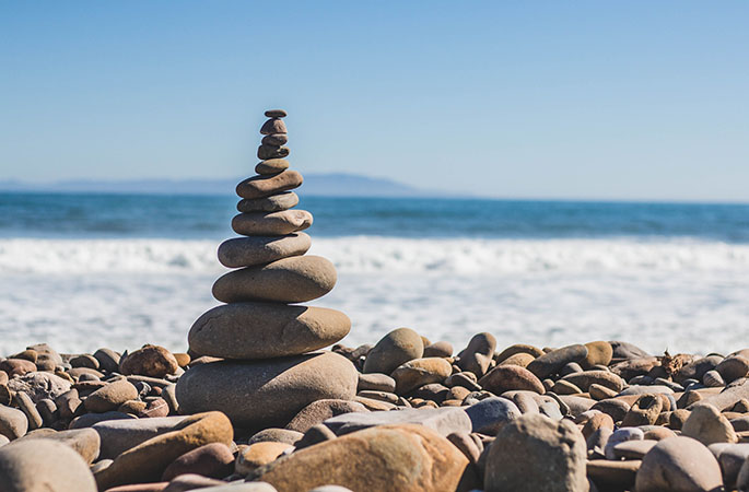 Rocks balancing on each other with a beach in the background.